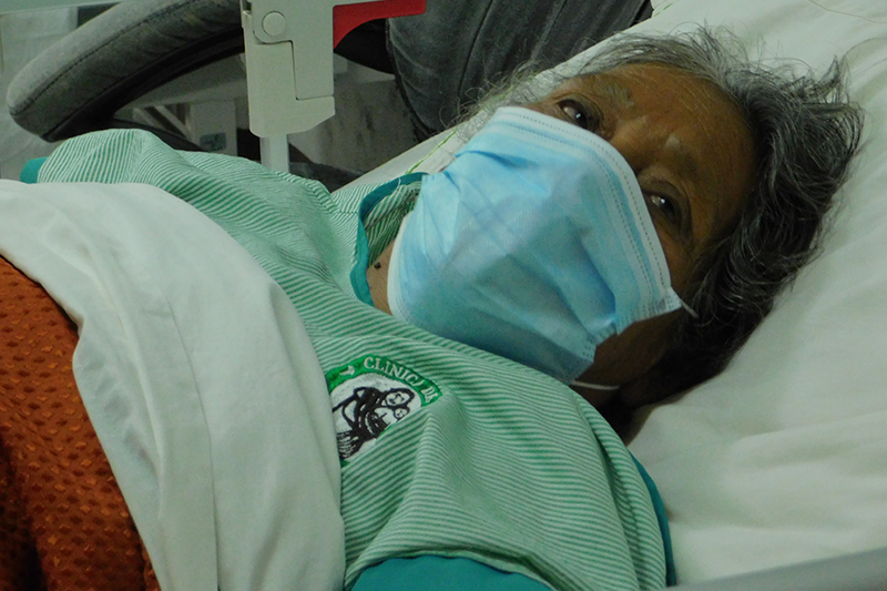 An elderly woman in a mask lies in a hospital bed